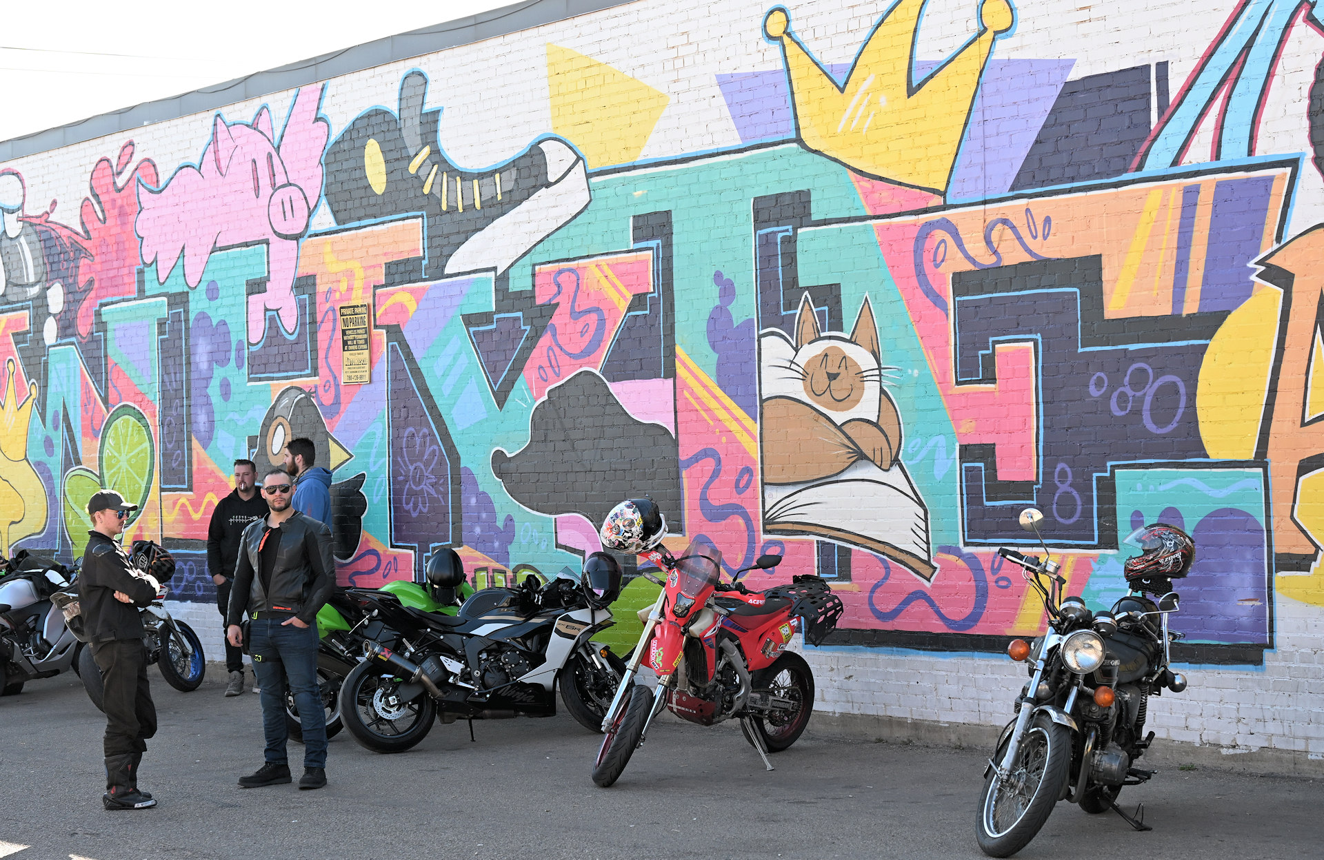 Vier Biker und eine Gruppe Motorräder die vor einem farbenfrohen Graffiti in Edmonton parken 