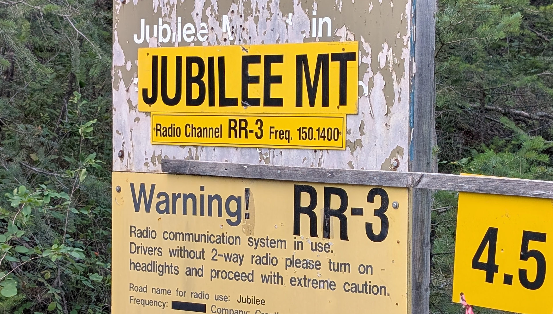 Gelbe Tafel die in Kanada beim Beginn von einem Waldweg über RR Funk Kanäle mit Frequenzen informiert. 