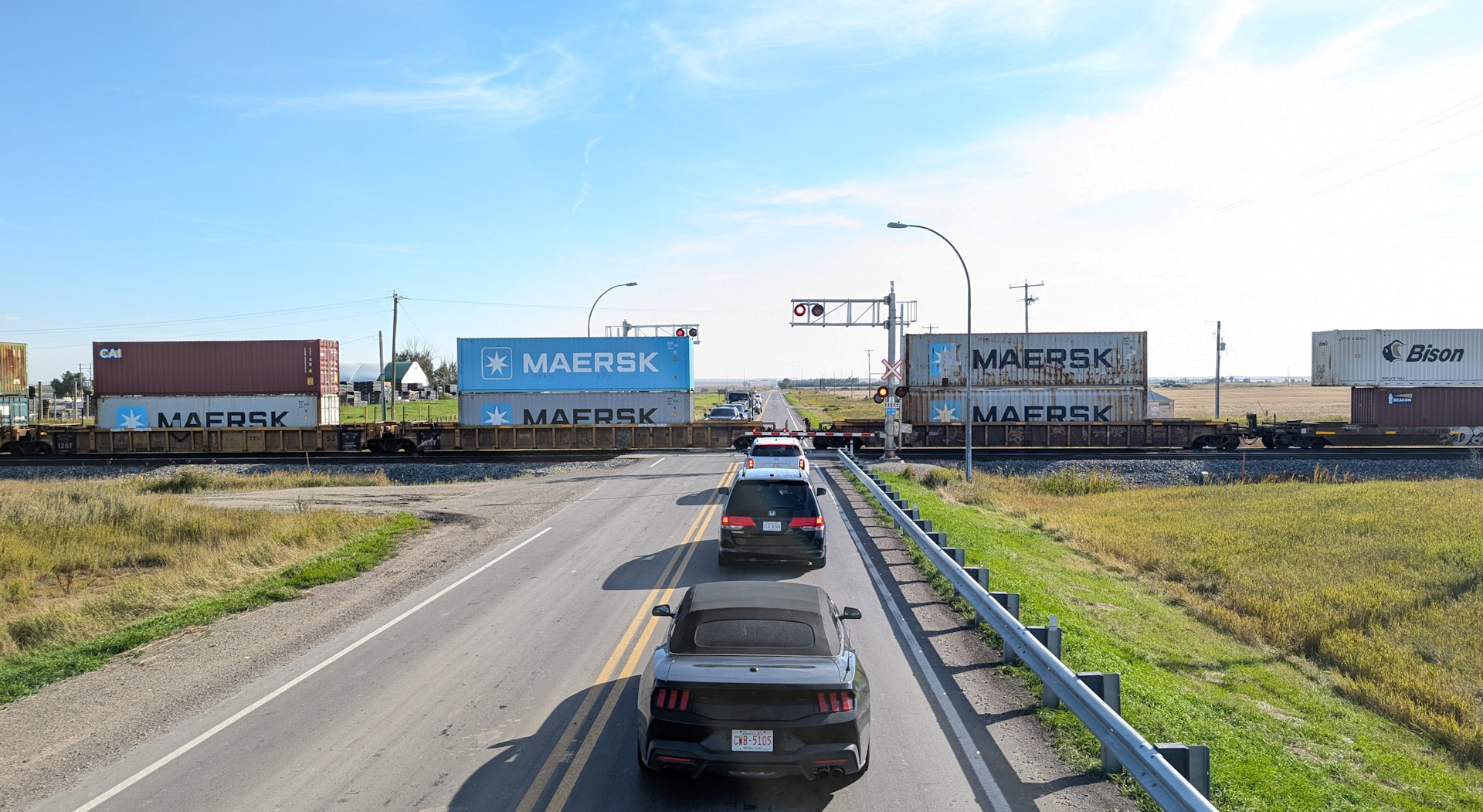 Bahnübergang in Alberta an dem ein Güterzug vorbei fährt und einige Autos warten 