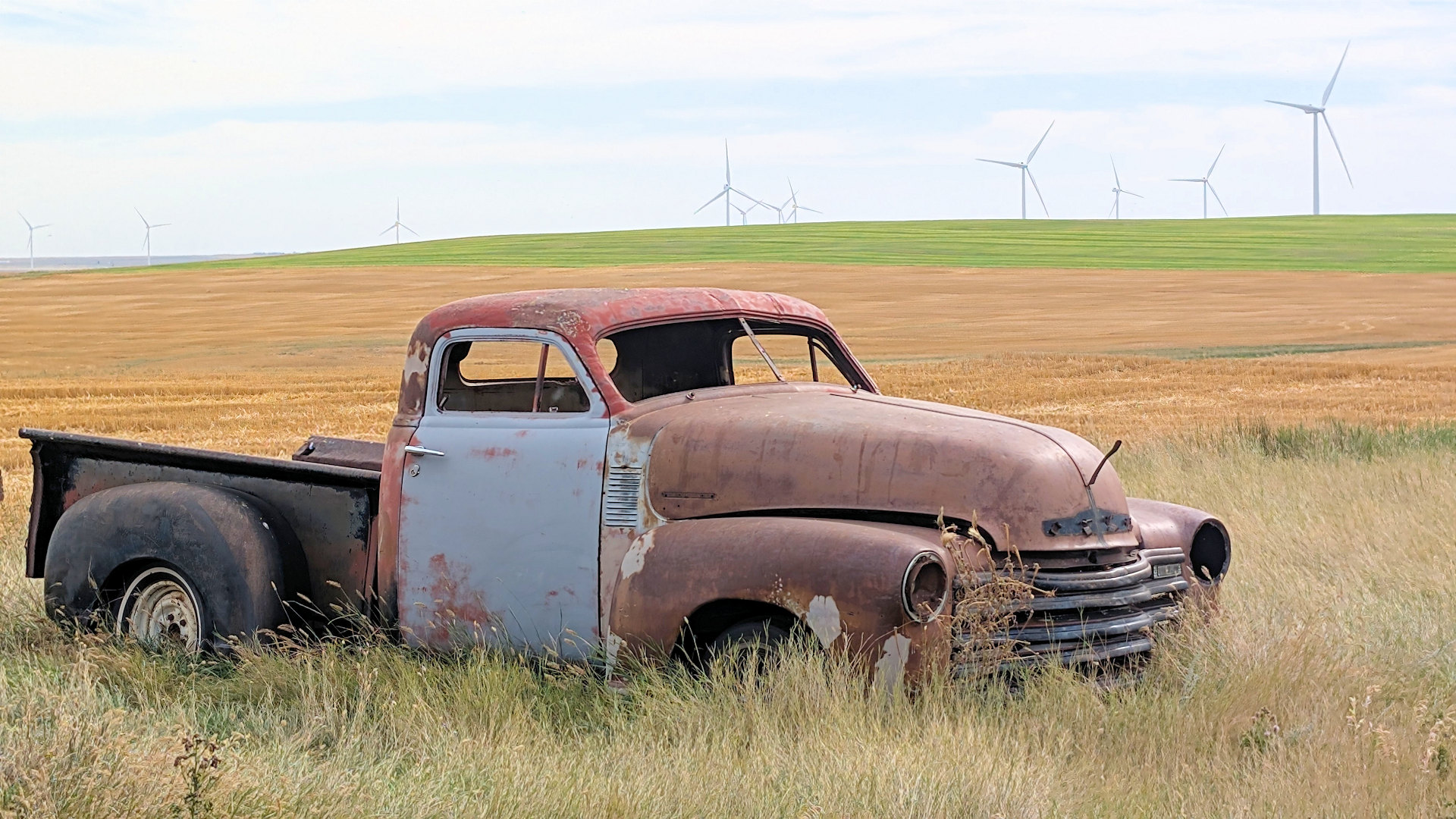 Verrosteter historischer Pickup Truck vor einem Feld mit Windrädern im Hintergrund 