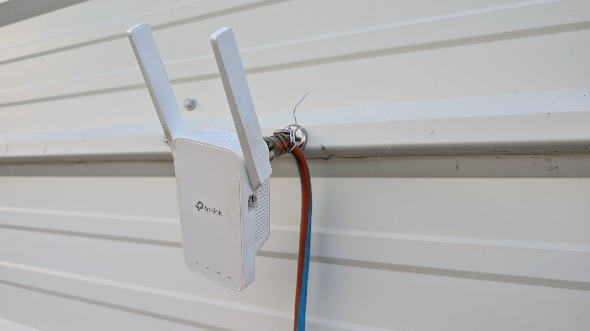 Weisser WLAN Extender hängt improvisiert mit einem Magneten befestigt an einer weissen Blechwand
