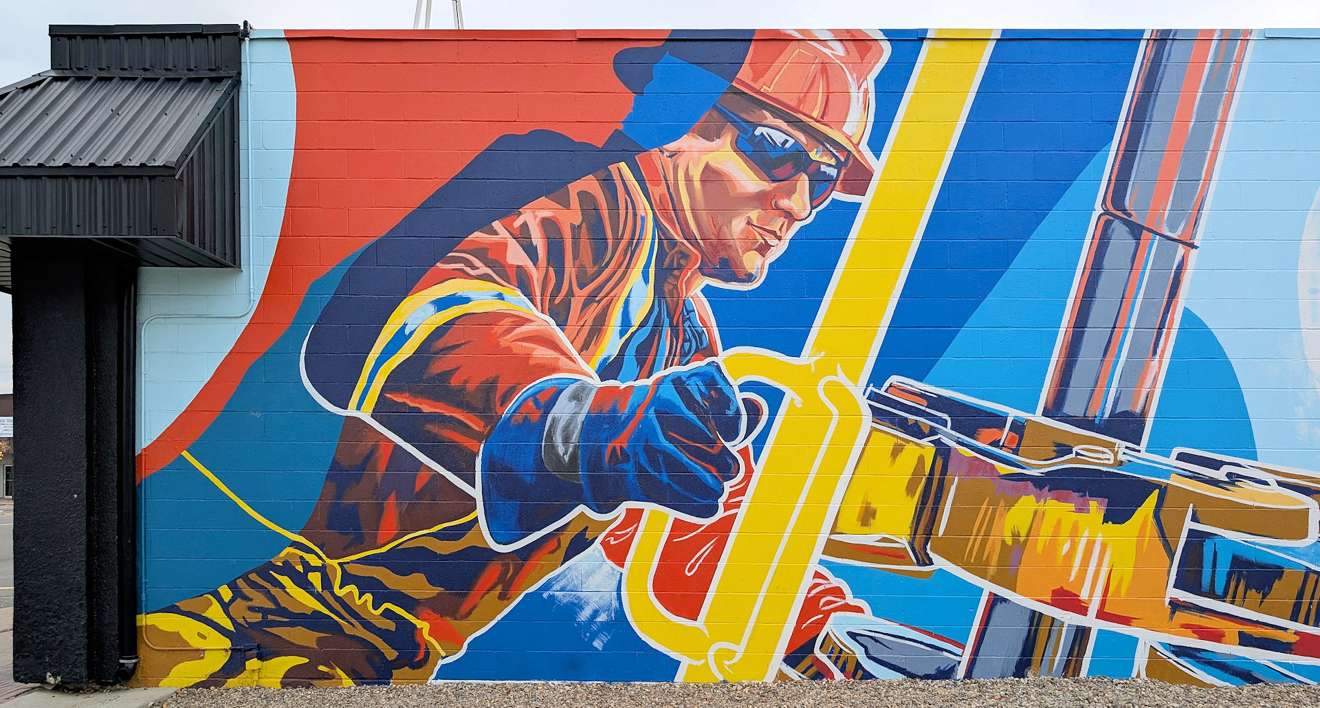 Wandbild in Taber was einen Ölfeldarbeiter mit Industrieausrüstung in leuchtenden Orange Blau Gelb und Rot Farben zeigt