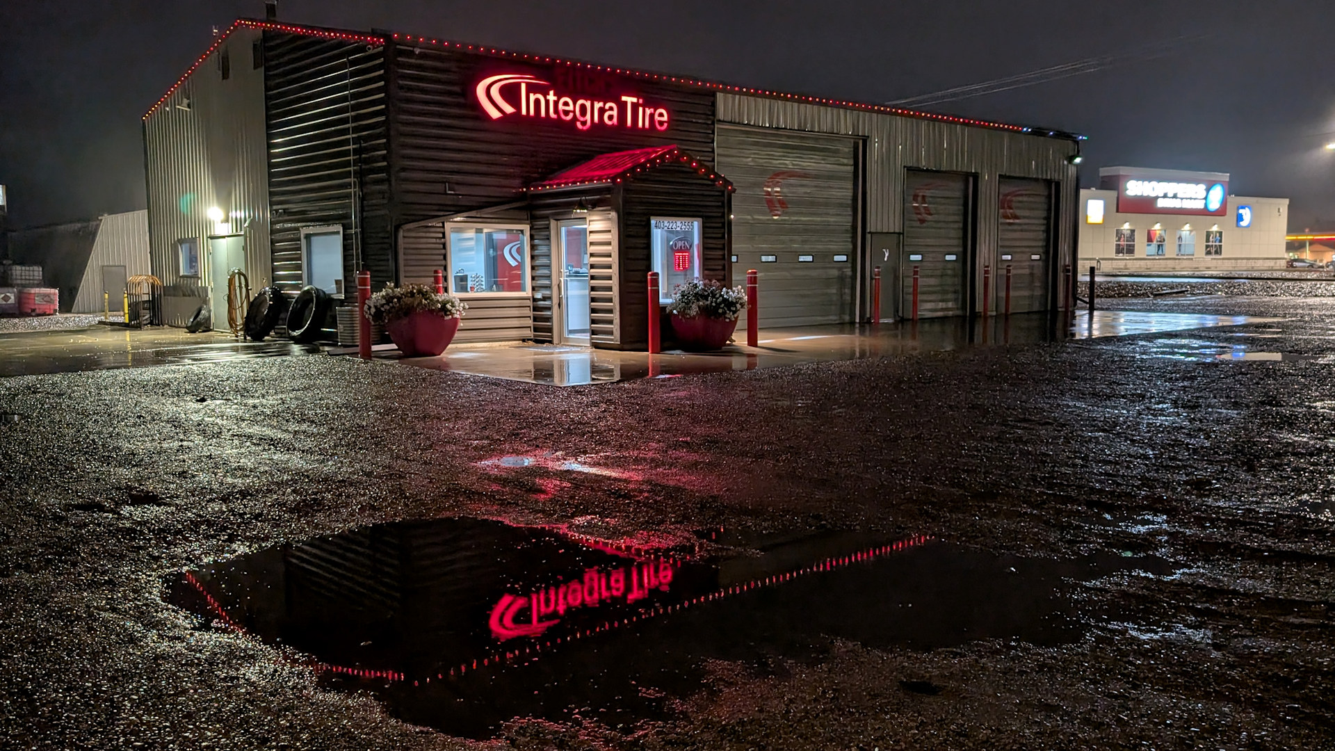 Integra Tire Laden in Taber der sich Nachts rot auf dem nassen Parkplatz in einer Pfütze spiegelt