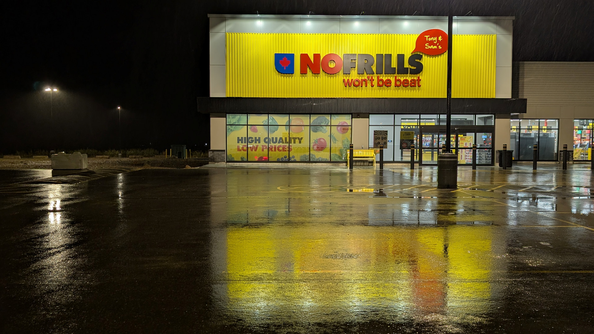NoFrills Filiale in Taber, die sich Nachts gelb auf dem nassen Parkplatz spiegelt
