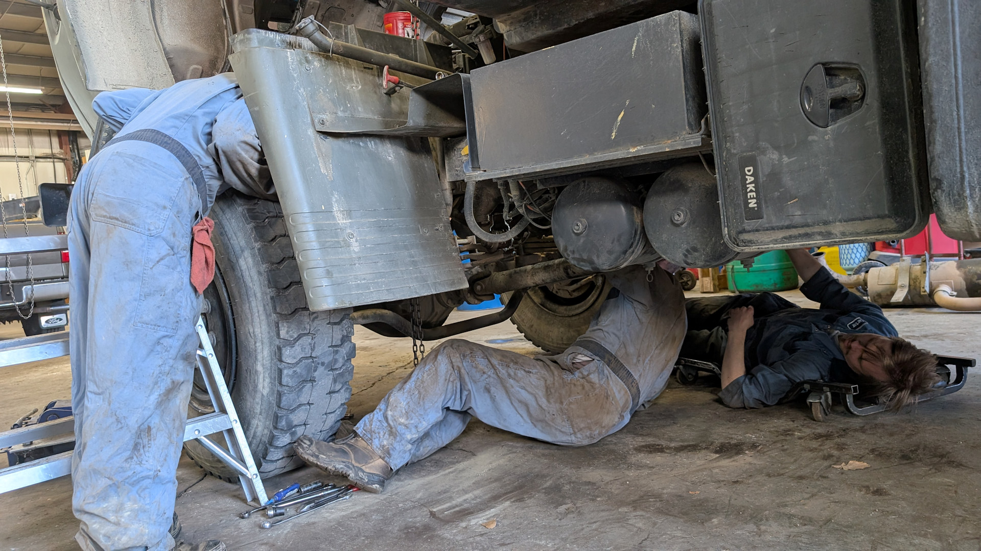 Drei Mechaniker in blauen Overalls arbeiten gleichzeitig an einem LKW