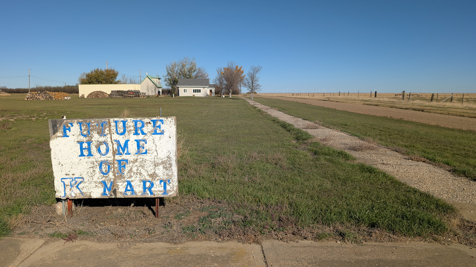 Schild in Nemiskam Kanada vor einem leeren Grundstück auf dem in verwitterter blauer Schrift Future Home of K Mart steht. 
